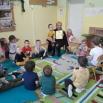 Pani Beata czyta grupie przedszkolaków siedzących na kolorowym dywanie w kręgu