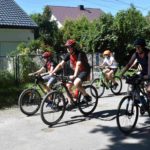 Czteroosobowa rodzina jadąca na rowerach, w tle domy
