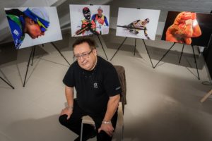 Autor wystawy fotografii duch sportu siedzący na krześle wśród swoich prac fotografia Dariusza Machury