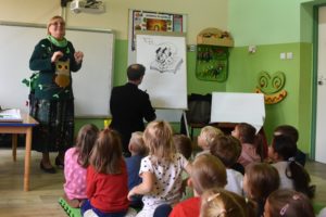 Dzieci słuchające Ewy Stadtmuller w trakcie spotkania, w tle rysownik Łukasz Zabdyr